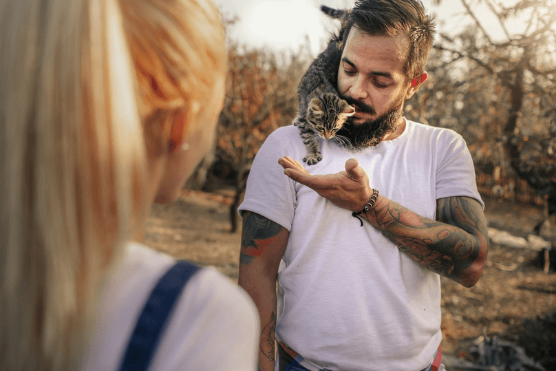 Tattooed Couple On Farm Together. Man carrying cute kitten on his shoulder.