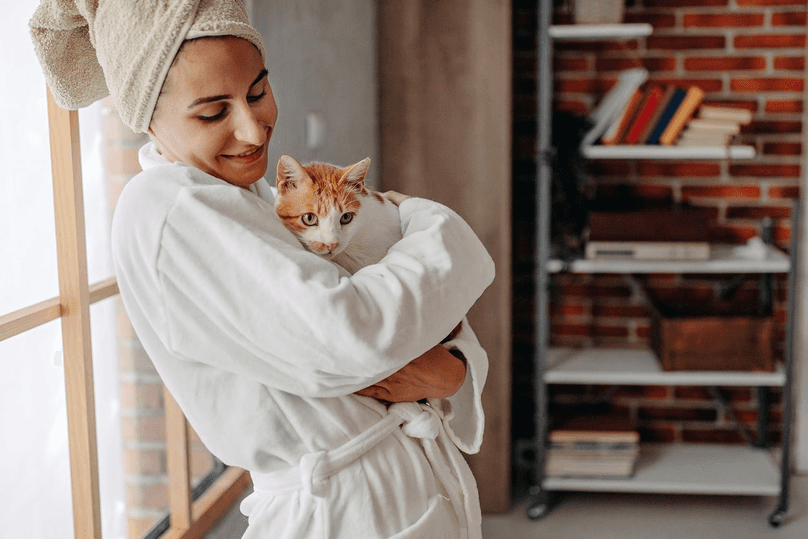 woman standing in front of window in robe holding her cat