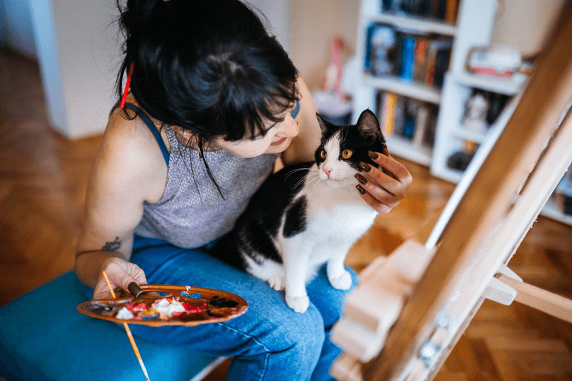 Portrait of a beautiful female artist painting in her studio with a cat in her lap