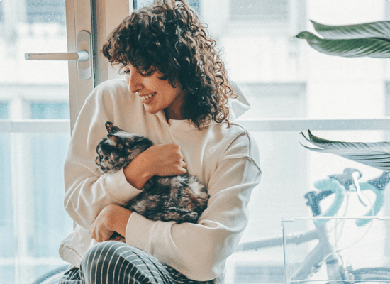 Cat being hugged by its owner near a window.